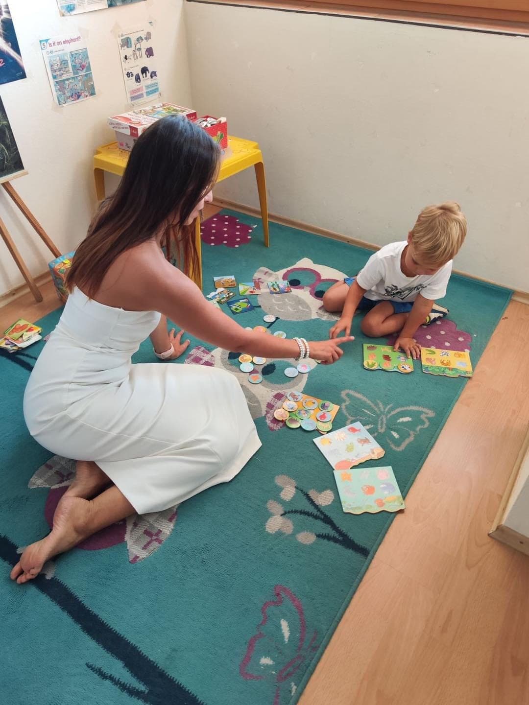 An adult and a child playing with picture cards on a rug, in a room set up with toys.